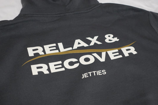 Close-up angled shot of the Relax & Recover back graphic showing the white lettering and gold wave detail on a gray hoodie.