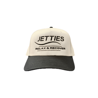 JETTIES Relax & Recover snapback hat with black brim — structured beige crown and embroidered logo, front view.