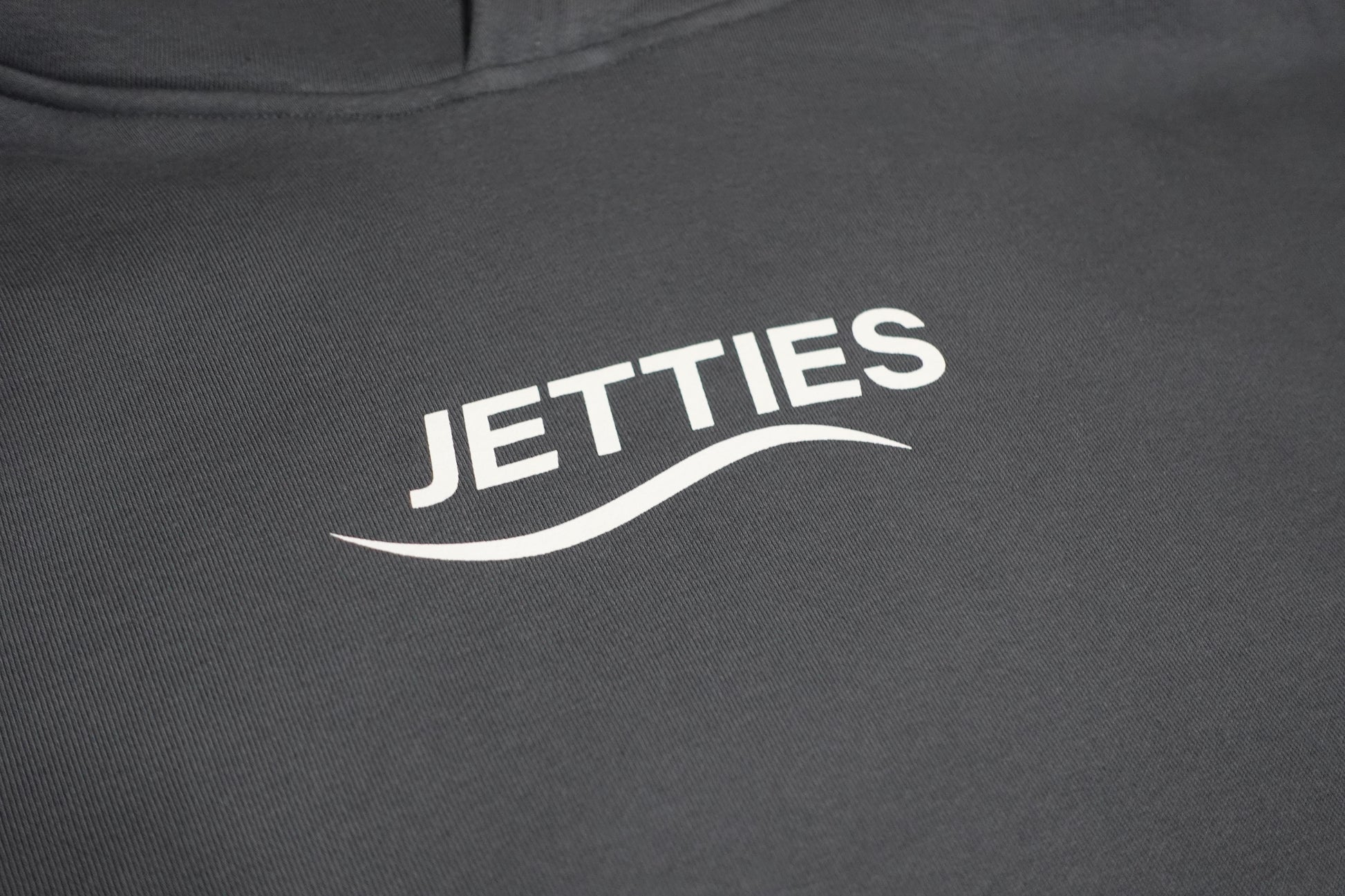 Close-up shot of the JETTIES chest logo printed in white on the gray hoodie.