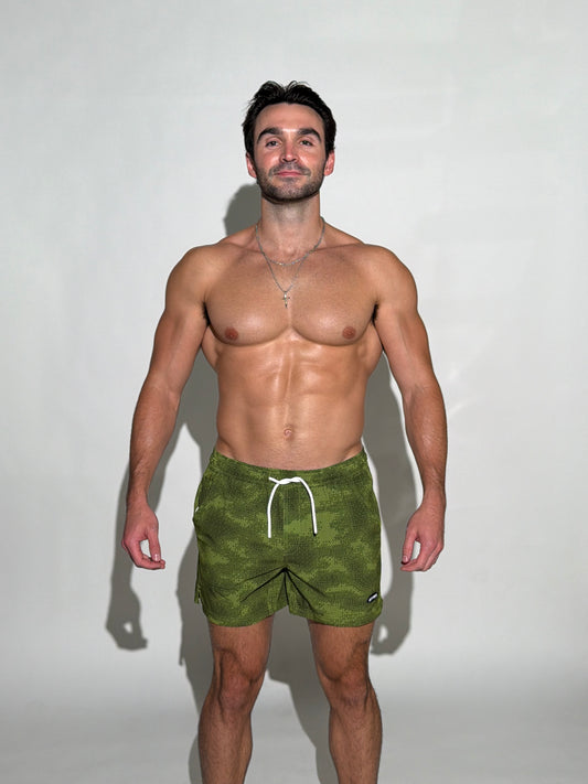 Model wearing the Woodsmen, green and black digital pixel camo mens bathing suit