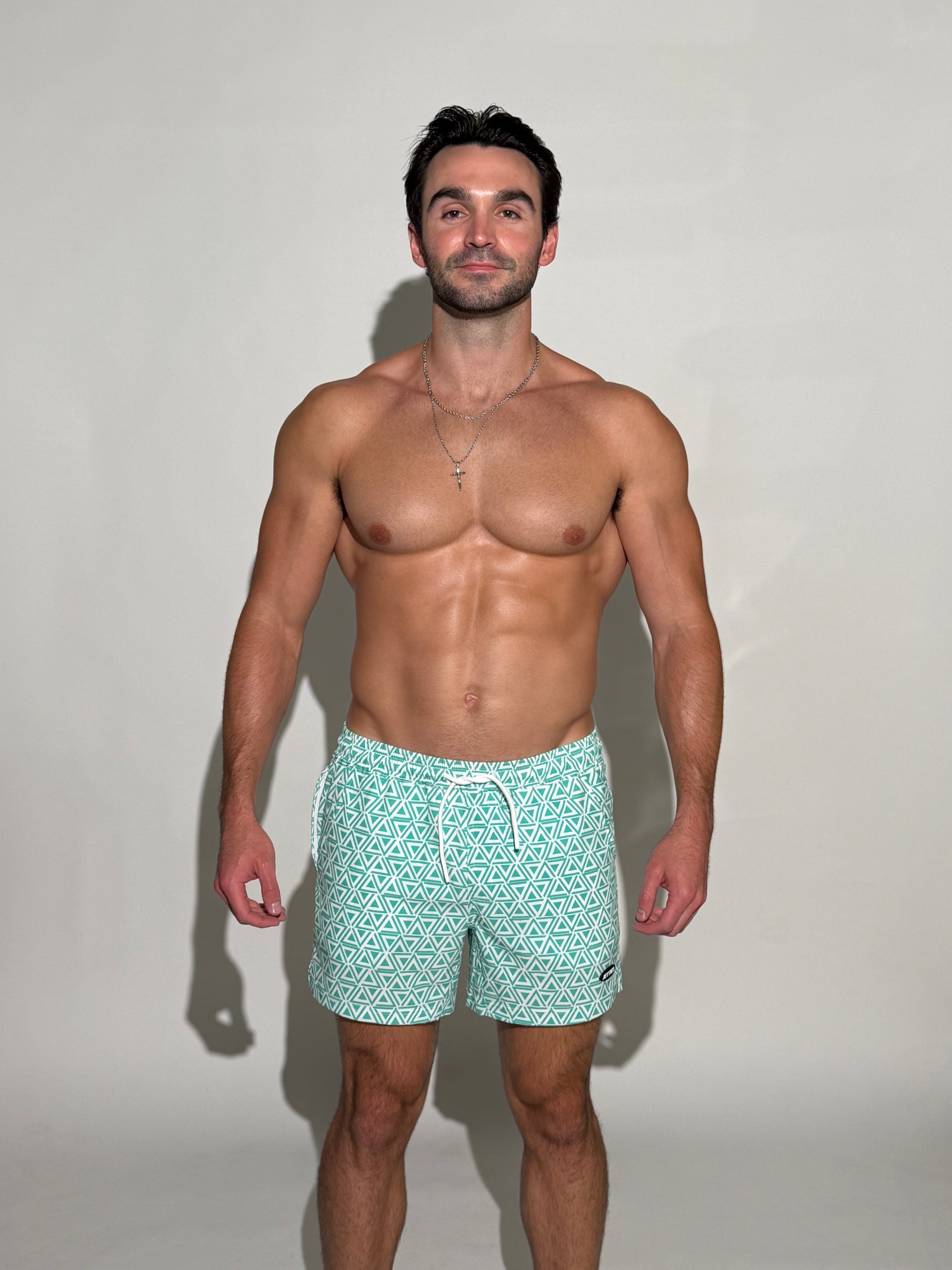Model wearing the JETTIES Delta Teal, Teal Blue and white triangle mens bathing suit, geometric pattern