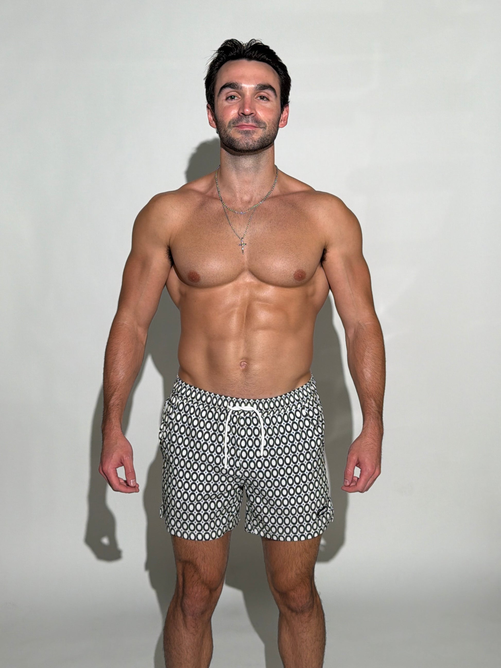 Model wearing the JETTIES Echo Charcoal, black and white circles mens bathing suit, geometric pattern