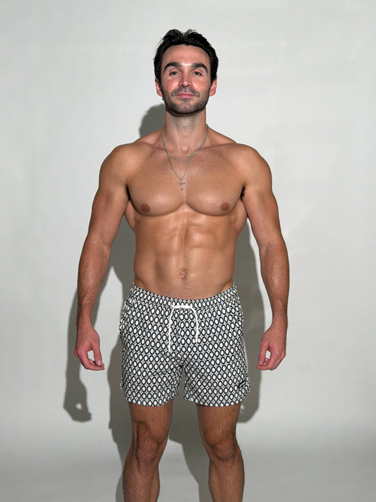 Model wearing the JETTIES Echo Charcoal, black and white circles mens bathing suit, geometric pattern