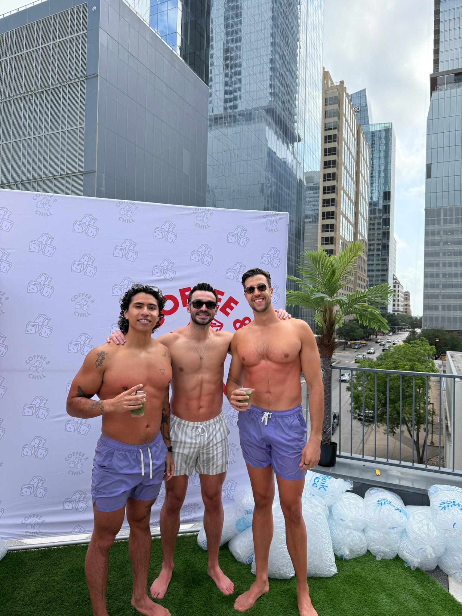 Three men posing together on a rooftop in JETTIES LAVENDER WAVE & CODE GRAY PLUNGE SHORTS bathing suits.