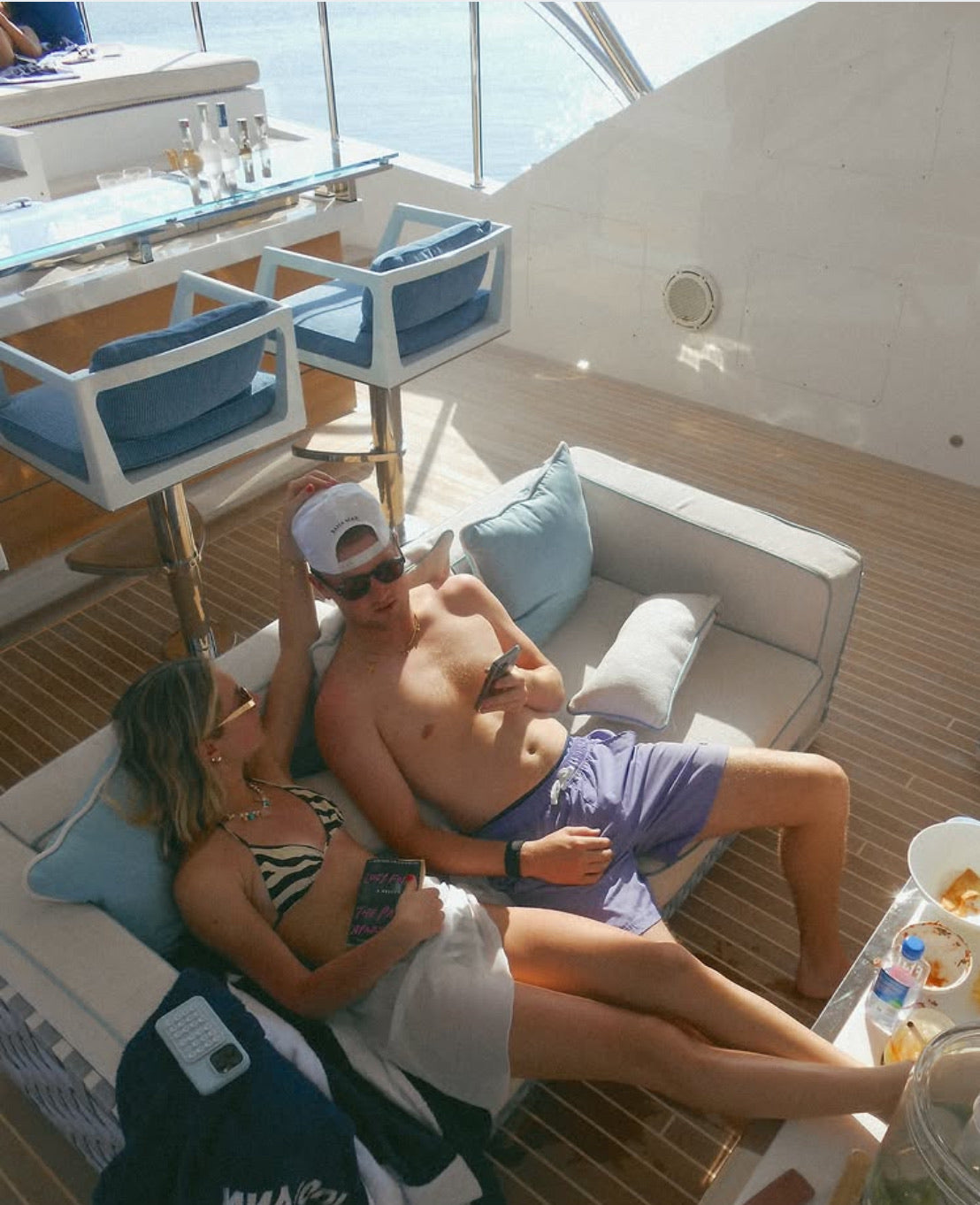 Couple relaxing on a yacht with a scenic view while man wearing JETTIES LAVENDER WAVE PLUNGE SHORT bathing suit